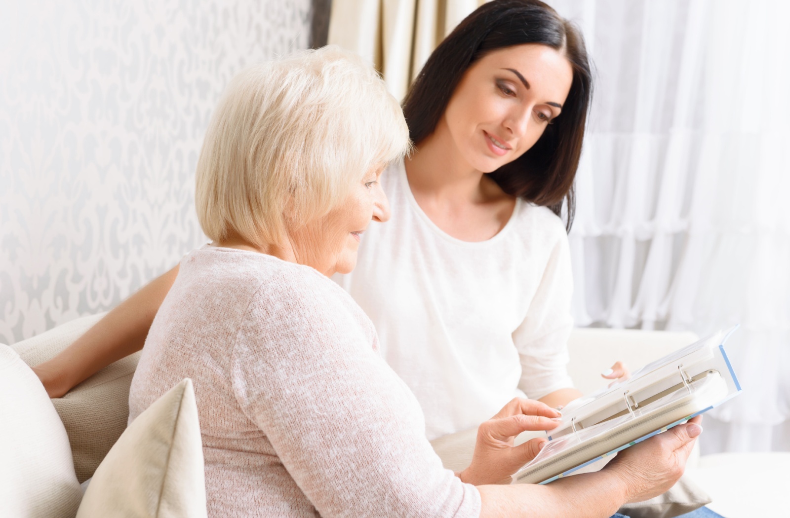 An adult daughter and her senior mother looking at a photo album and smiling.