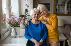 An adult woman hugging her senior mother and smiling.