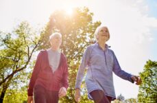 An elderly man and woman walking outdoors with the sun shining.