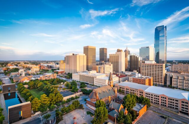 A wide angled overhead shot of the Oklahoma City skyline with a bright blue sky in the background.