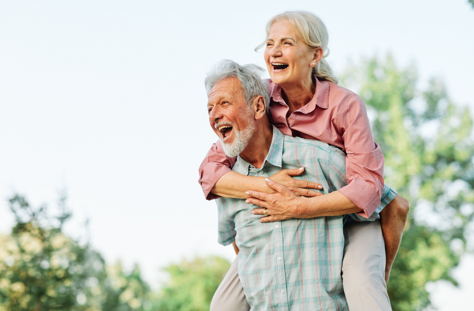 A senior woman laughing while her husband gives her a piggyback ride while walking outdoors in Oklahoma City.
