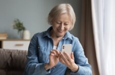 An older woman in memory care smiling while exploring a new dementia-friendly cell phone.