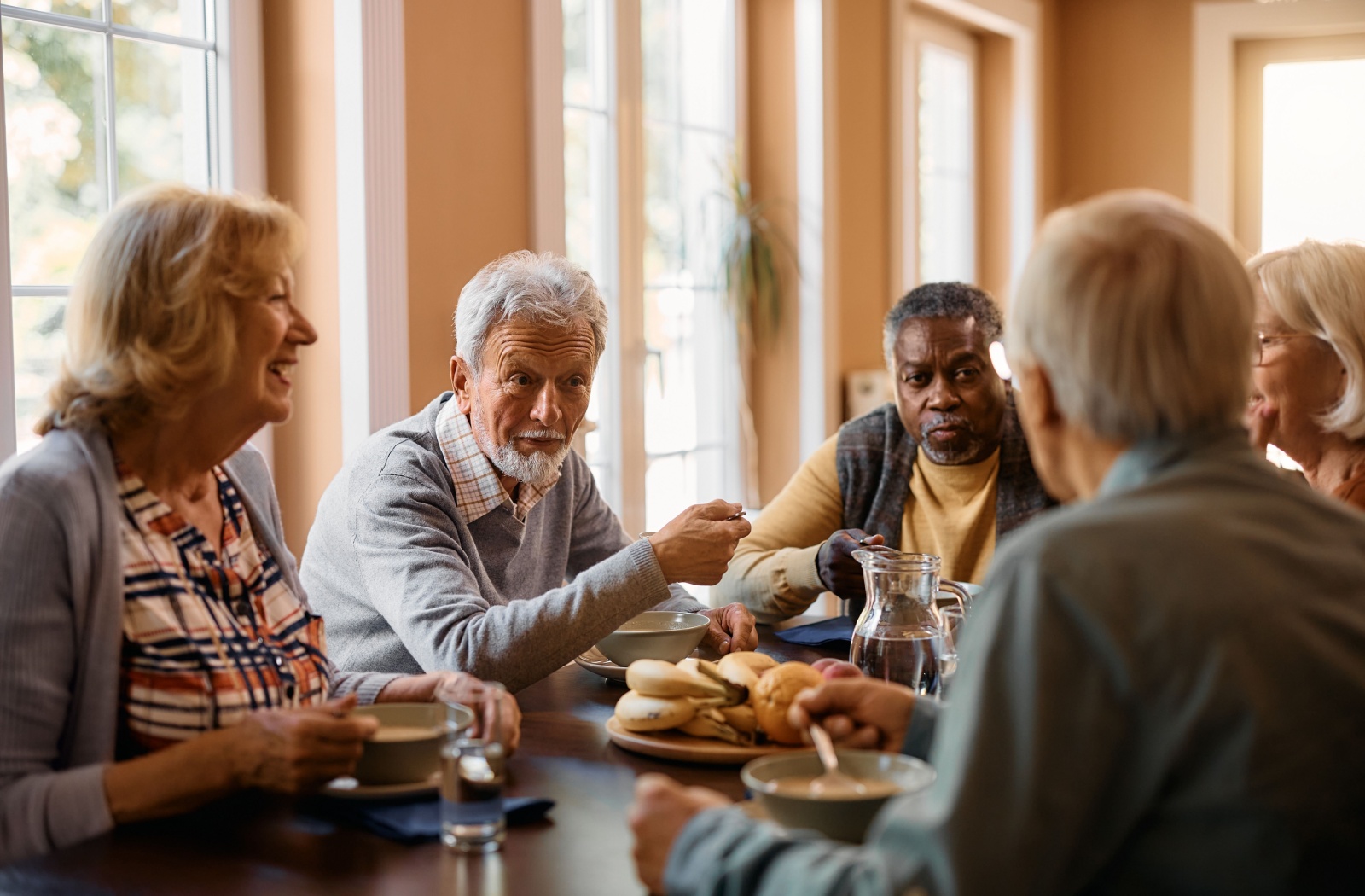 Seniors sitting around a table sharing a meal together in community.