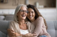 Senior person and younger adult embrace while sitting on a couch.